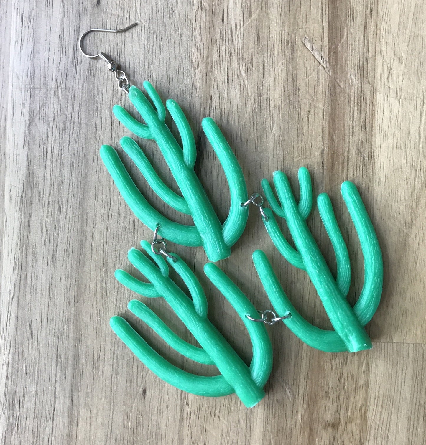 Three plastic cacti are linked by metal rings, for a giant bright earring.