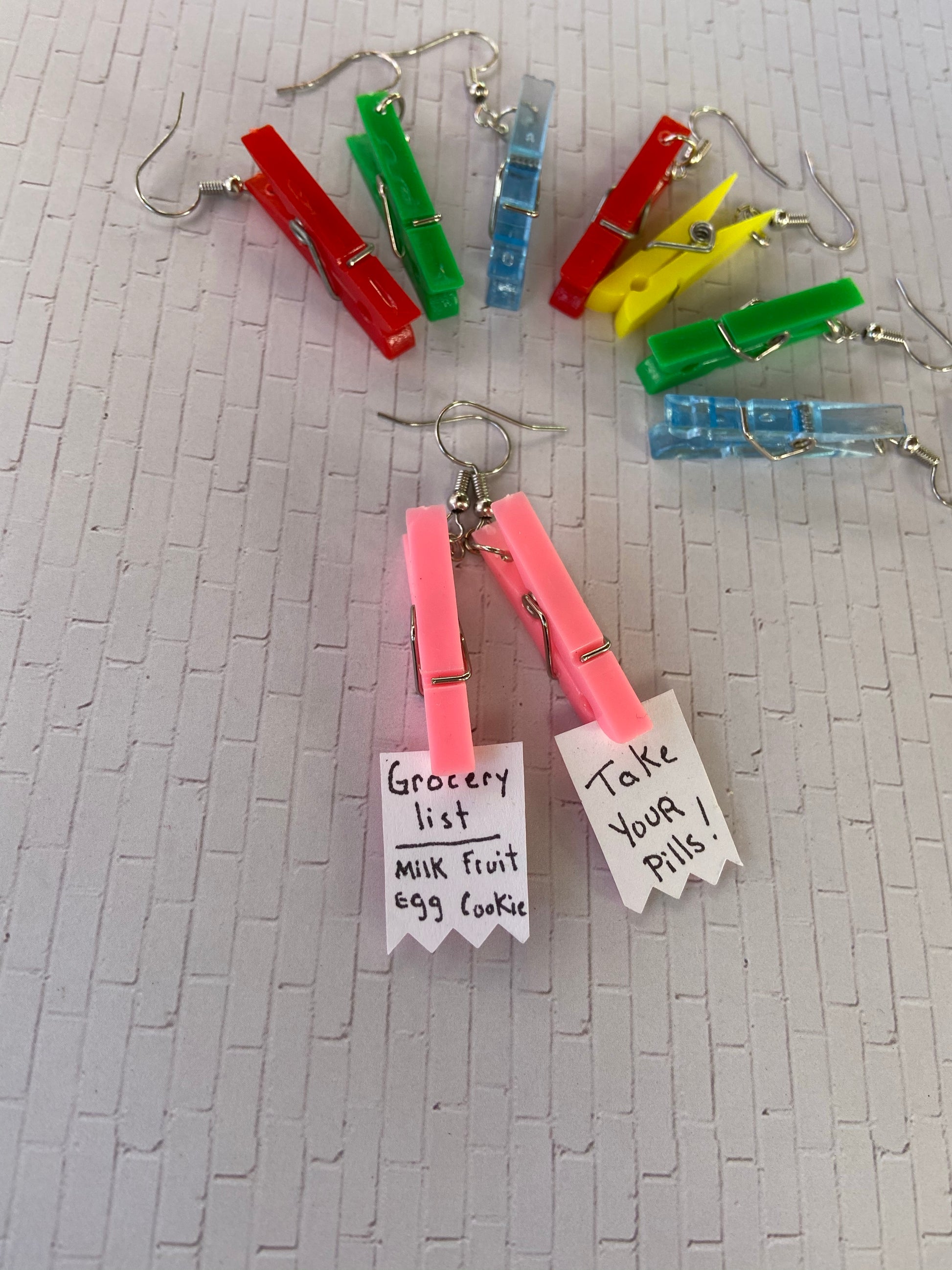 Notes to self earrings in a variety of colors ranging from pink to red to translucent blue to green to yellow.
