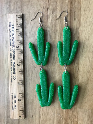 Cacti earrings rest next to a ruler which shows their length to be 5 1/2 inches.
