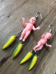 A vintage baby charm hovers above two dangling ears of corn.  