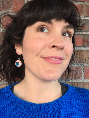 Model leans against a brick wall while modeling blinking doll eye earrings.